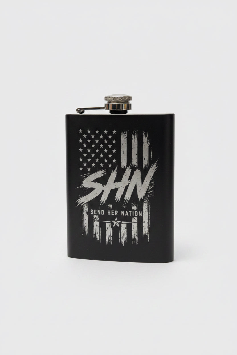 A matte black insulated flask with a silver screw-top lid, featuring a distressed white American flag graphic and the text 'SHN' and 'SEND HER NATION,' 